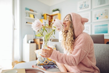 A woman in pink loungewear smells some flowers at home on Valentine's Day.