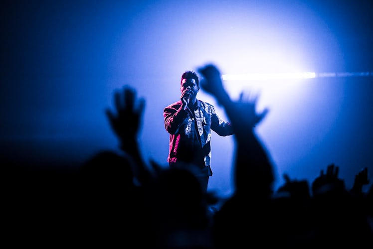 The Weeknd performs to a small crowd of people while his stage is lit up blue and pink.