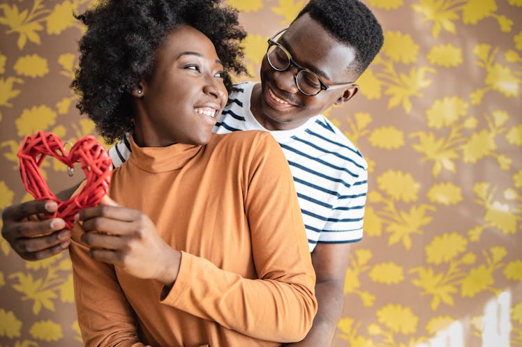 A cute couple holds onto a red heart, while at home celebrating Valentine's Day.