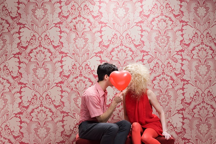 A young couple kisses behind a heart-shaped balloon in a throwback Valentine's Day picture.