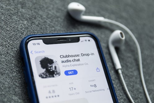 The Clubhouse Drop-in audio chat app is ready to be downloaded on a phone, with headphones sitting n...