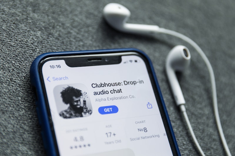 The Clubhouse Drop-in audio chat app is ready to be downloaded on a phone, with headphones sitting n...
