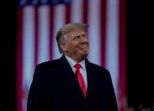 President Trump standing in front of an American flag banner.