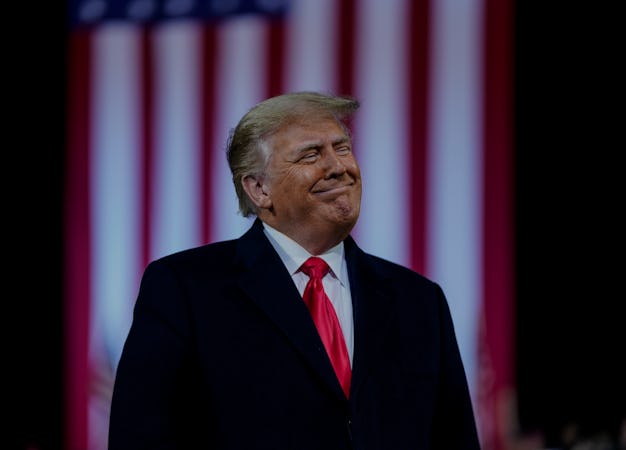 President Trump standing in front of an American flag banner.