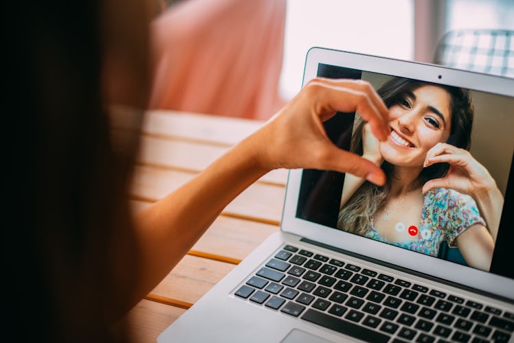 A best friend smiles on a laptop screen while making half of a heart and another friend completes it...