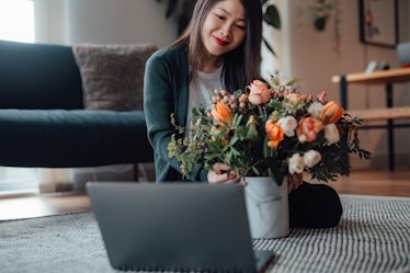 A smiling woman sits in front of her laptop with a beautiful bouquet of flowers while on a virtual V...
