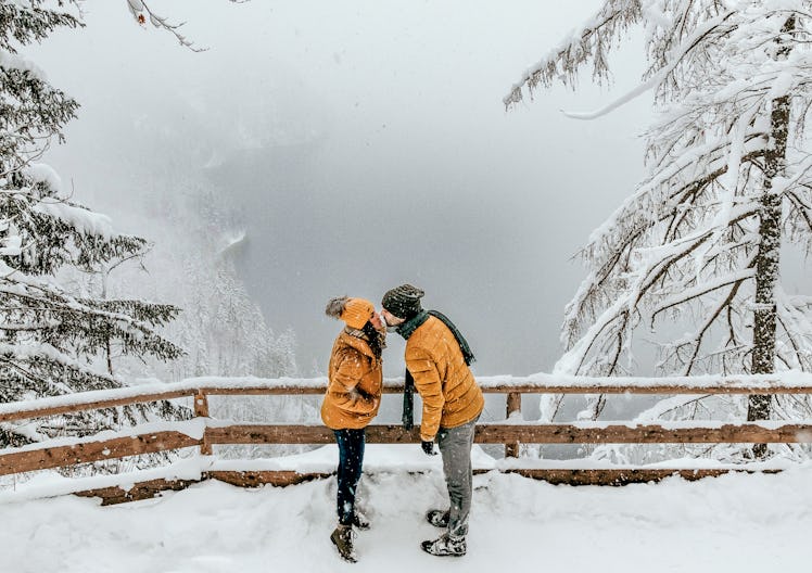 A couple kisses by a scenic overlook while on a snowy winter hike.