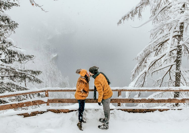 A couple kisses by a scenic overlook while on a snowy winter hike.