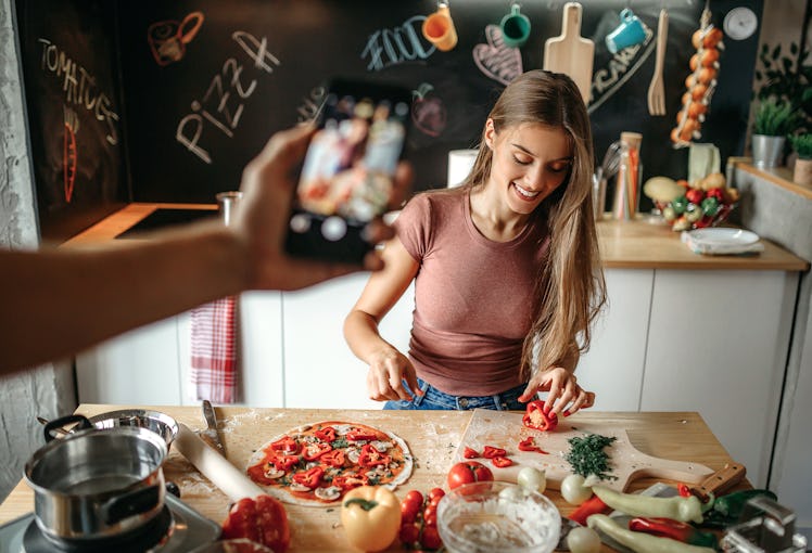 A woman cuts veggies for a pizza wrap while her partner takes a picture for TikTok.