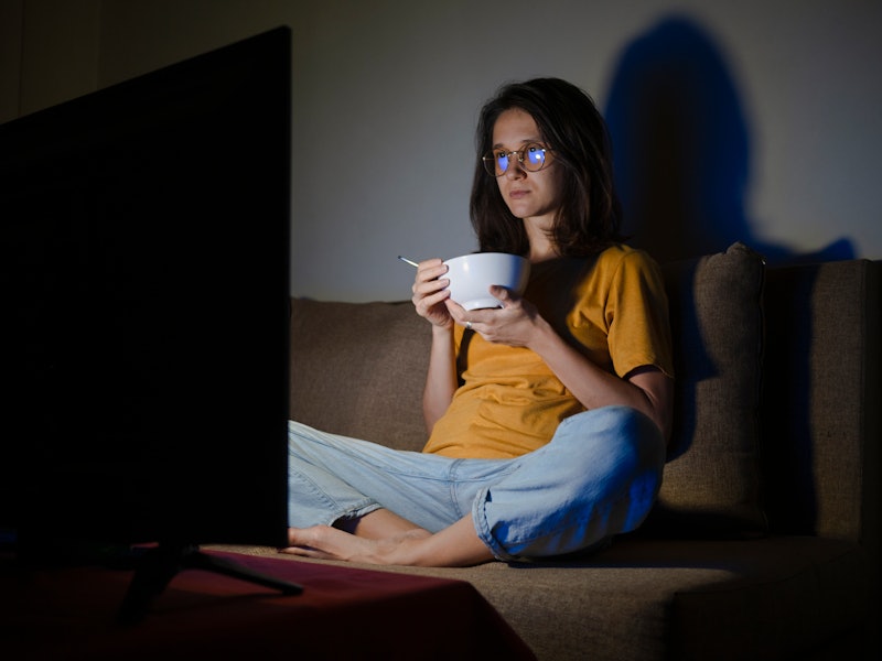 A woman watches escapist tv while eating a bowl of cereal.