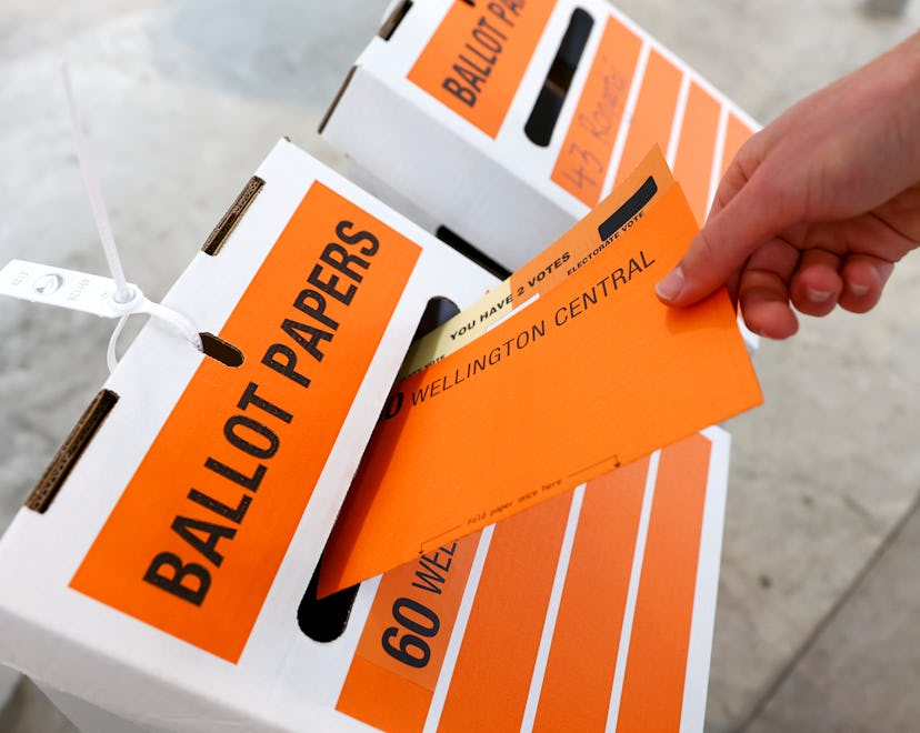 An orange ballot envelope is slipped into a white-and-orange collection box marked "ballot papers."