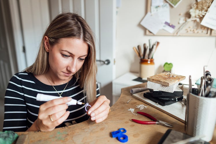 A woman crafts a ring uses glue and pliers for a fun DIY at home.