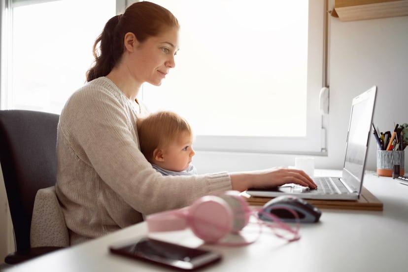 Woman working at computer with baby on lap, in a story about Women's History Month Facts.