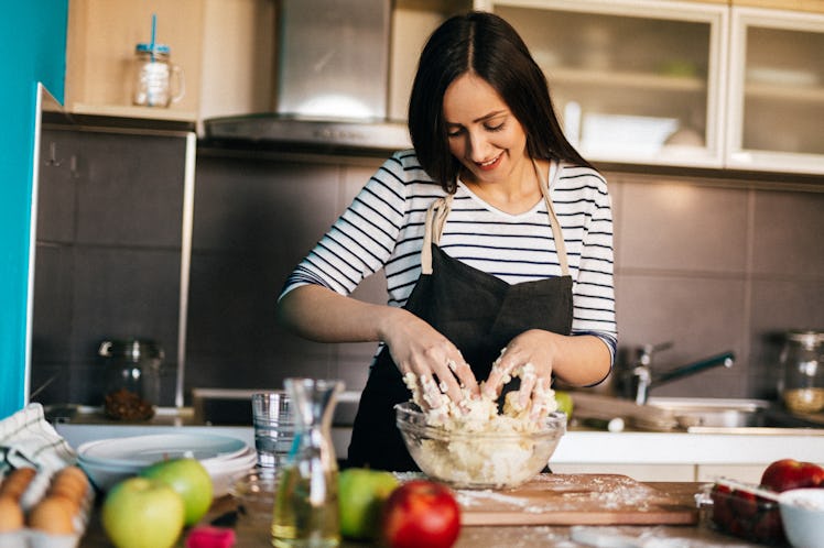 A happy woman kneads a flour and water dough in her kitchen.