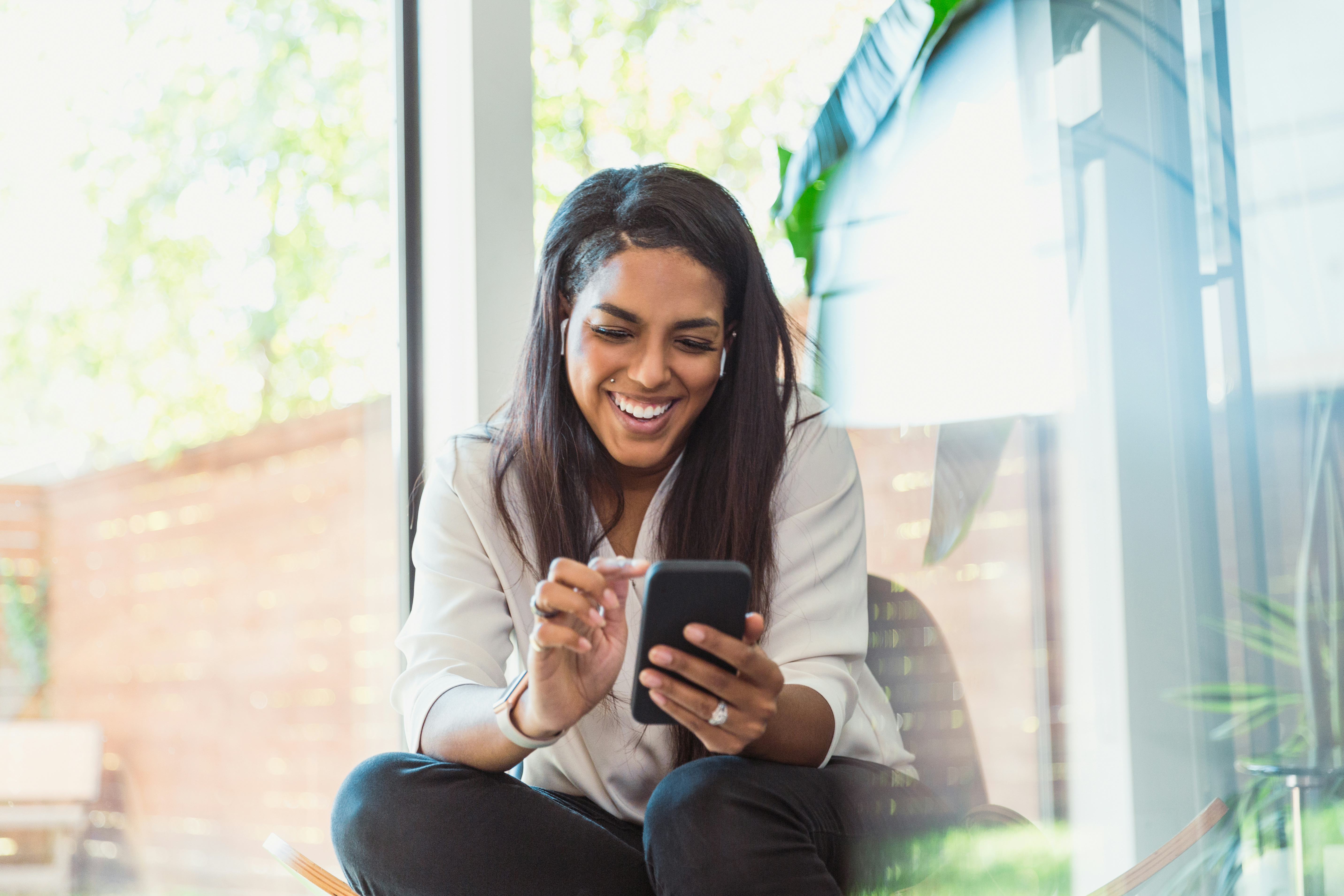 A woman looks at her phone laughing at Twitter's Super Follows feature.