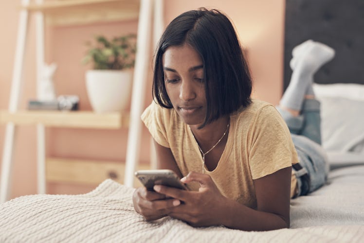 Shot of a young woman using a smartphone while relaxing on her bed at home