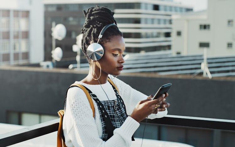 Shot of an attractive young woman using a smartphone to listen to music in the city
