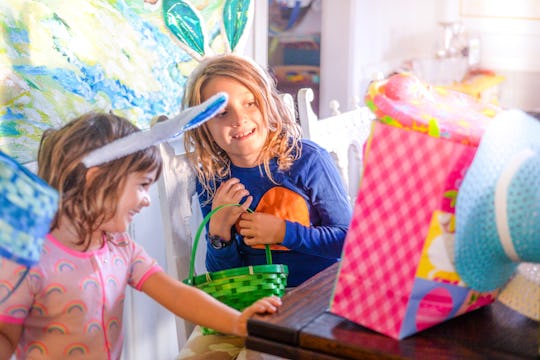 Adorable sisters wearing bunny ears in a candid family photo on Easter morning, they are surrounded by colorful Easter gifts and full of excitement and joy