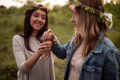 Two female friends with floral crowns breaking easter eggs.