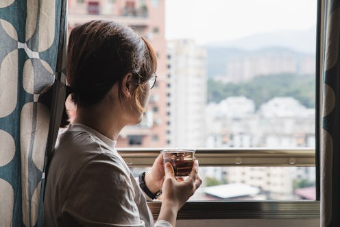asian woman holding a water glass and staring out of window