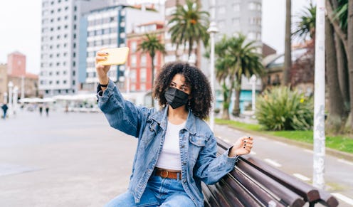 A young girl with afro hair wearing a face mask takes a selfie with the phone in the street. Here's ...