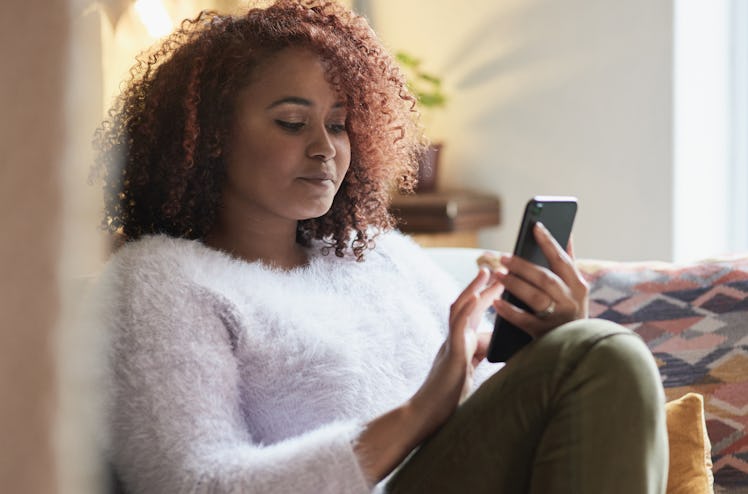 Shot of a young woman using a cellphone while relaxing at home