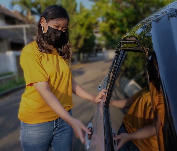 Candid shot of Asian young woman with a protective face mask, opening car door during Covid 19 pande...