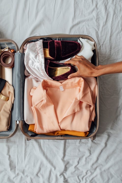 Hands of unrecognisable woman putting velvet loafers in her suitcase. Is it safe to travel once your...