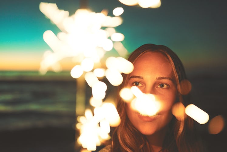 Shot of a young woman holding a sparkler at the beach at night