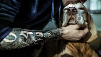 A tattooed man kissing his dog on the head