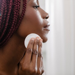 Beautiful African woman cleaning her face with cotton pad.
