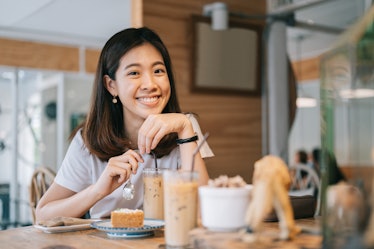 A happy woman enjoys a cake and iced latte at a coffee shop. 