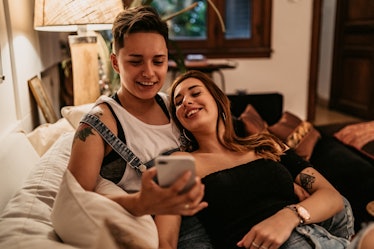 Young beautiful lesbian couple spending time on the couch at home with smartphone.