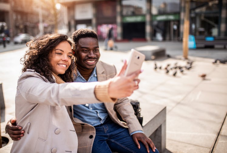Happy young African American couple taking a photo together in the city.