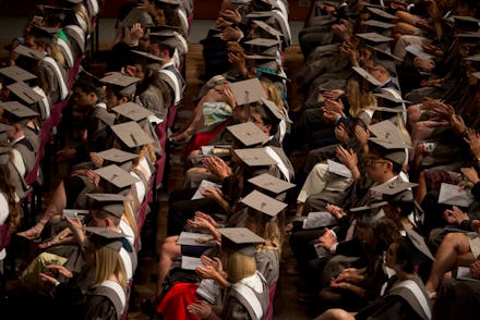 Young graduates wearing rented gowns and mortarboards applaud a speech in the central hall of their ...