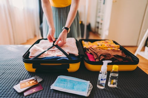 Woman packing suitcase for business travel including face masks and airplane travel-sized antibacter...
