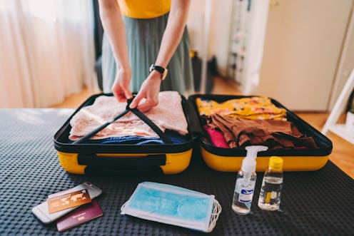 Woman packing suitcase for business travel including face masks and airplane travel-sized antibacter...