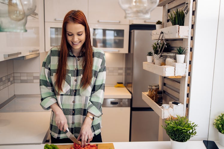 A woman wearing a green flannel cuts up vegetables in her kitchen.