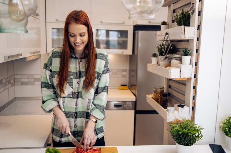 A woman wearing a green flannel cuts up vegetables in her kitchen. 