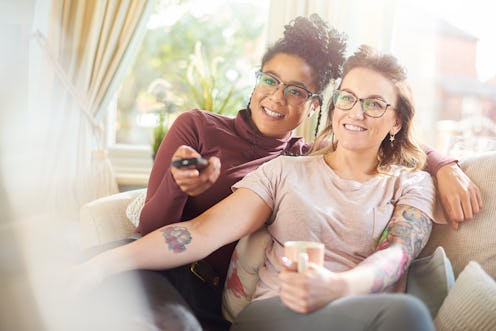 a female same sex couple sit on the sofa watching tv together