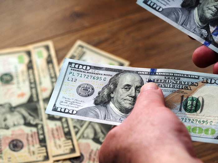 In this photo illustration, hands are seen counting US 100 dollar bills.