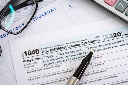 A 1040 form for the 2020 tax year is seen laid out on top of a calendar along with a pen, calculator...