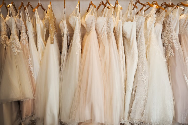 Several wedding dresses with appliqué, lace, and floral detailing are displayed on a rack.