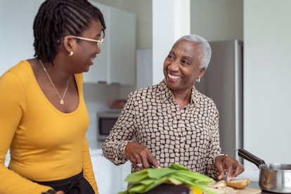 A beautiful black senior woman is cooking with her granddaughter. They are enjoying the special bonding time together as the grandmother slices vegetables.