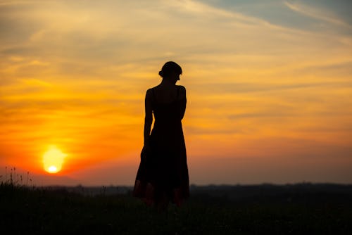 A woman is silhouetted standing in sunset. Trauma can be hard to define.