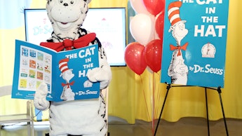 Dr. Seuss mascot holding "The Cat in the Hat" book with a banner and balloons in the background