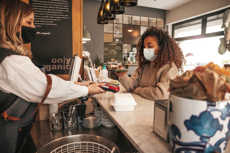 A person wears a mask while ordering coffee. Keeping social interactions outdoors is safest even aft...