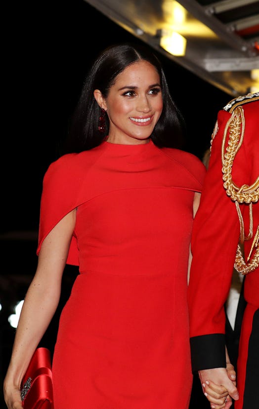 Meghan Markle with a signature hairstyle at an event in a red dress holding her husband, Prince Harr...