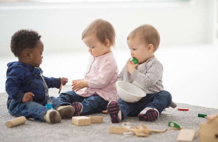 A group of adorable 1-2 year olds sit on a carpet and play with blocks.