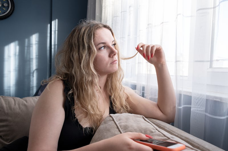 Sad young woman using mobile phone on sofa. Horizontal composition.